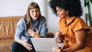 Two young businesswomen having a discussion while looking at a laptop screen