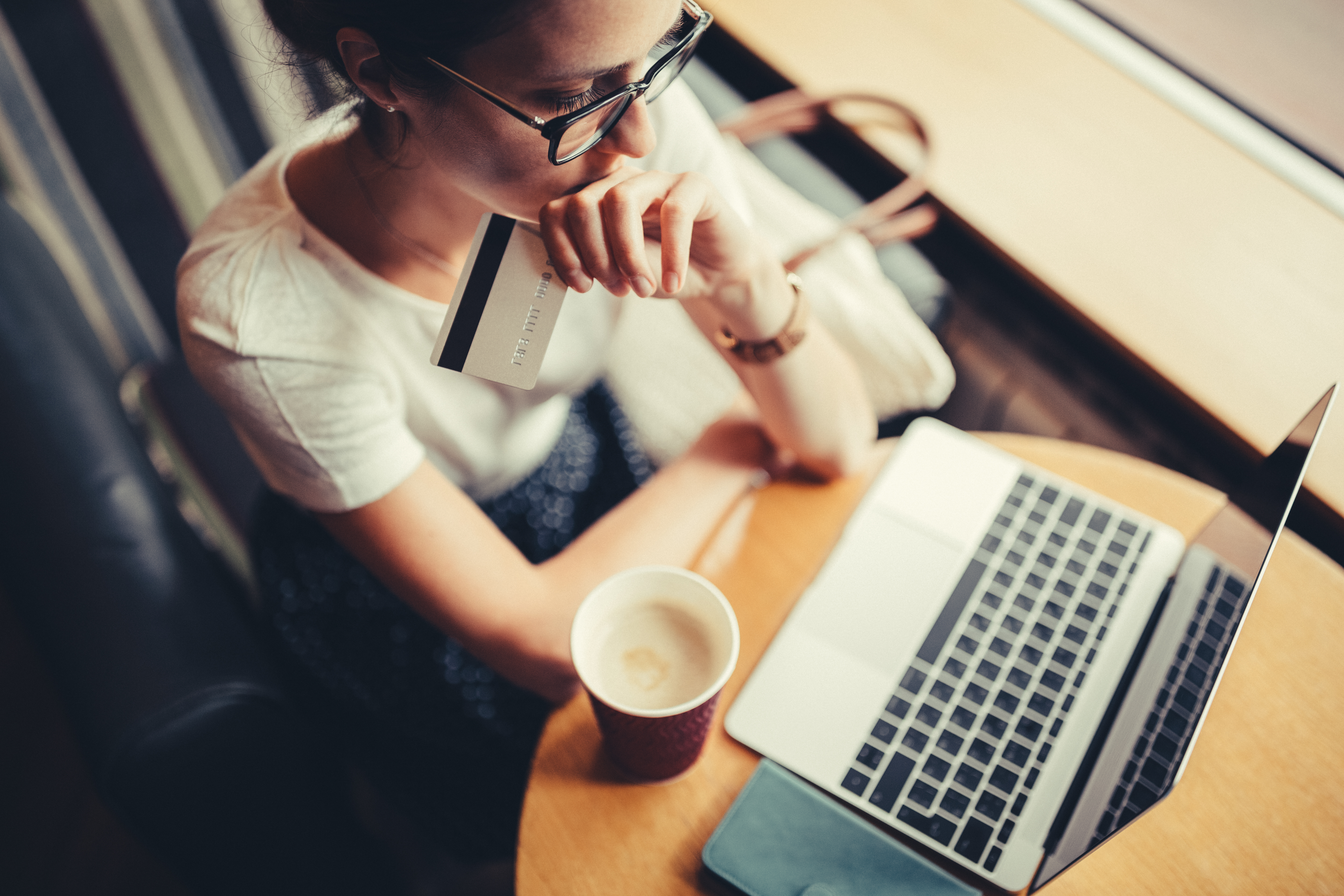 A women looking at her laptop with a credit card in her hand and coffee on the table