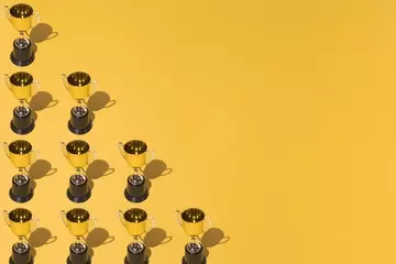 An array of gold trophies stacked in a pyramid shape on a golden background. 