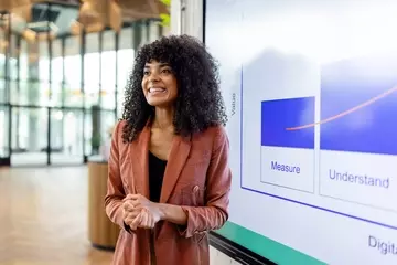 Woman smiling in front of presentation on a screen.