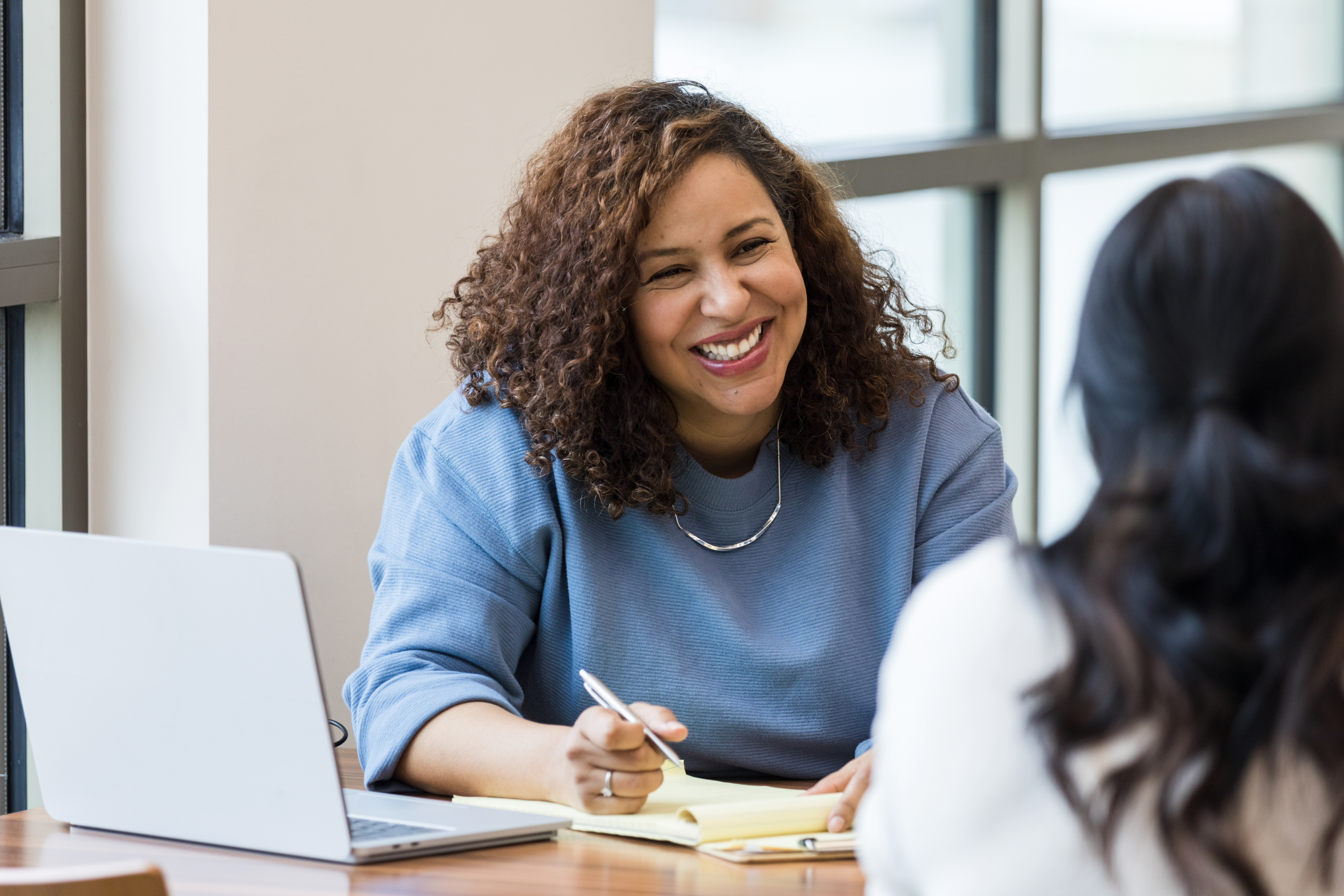 Woman with computer and pen in hand interviewing job candidate.