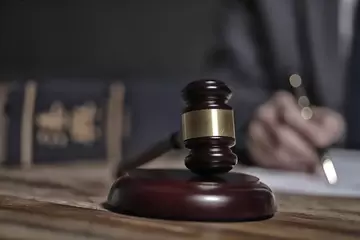 A gavel appears in the foreground with a hand holding a pen behind it. 