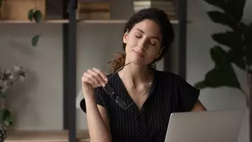 Calm latina woman relax at desk take break from computer work hold eyewear in hand give rest to tired eyes. 